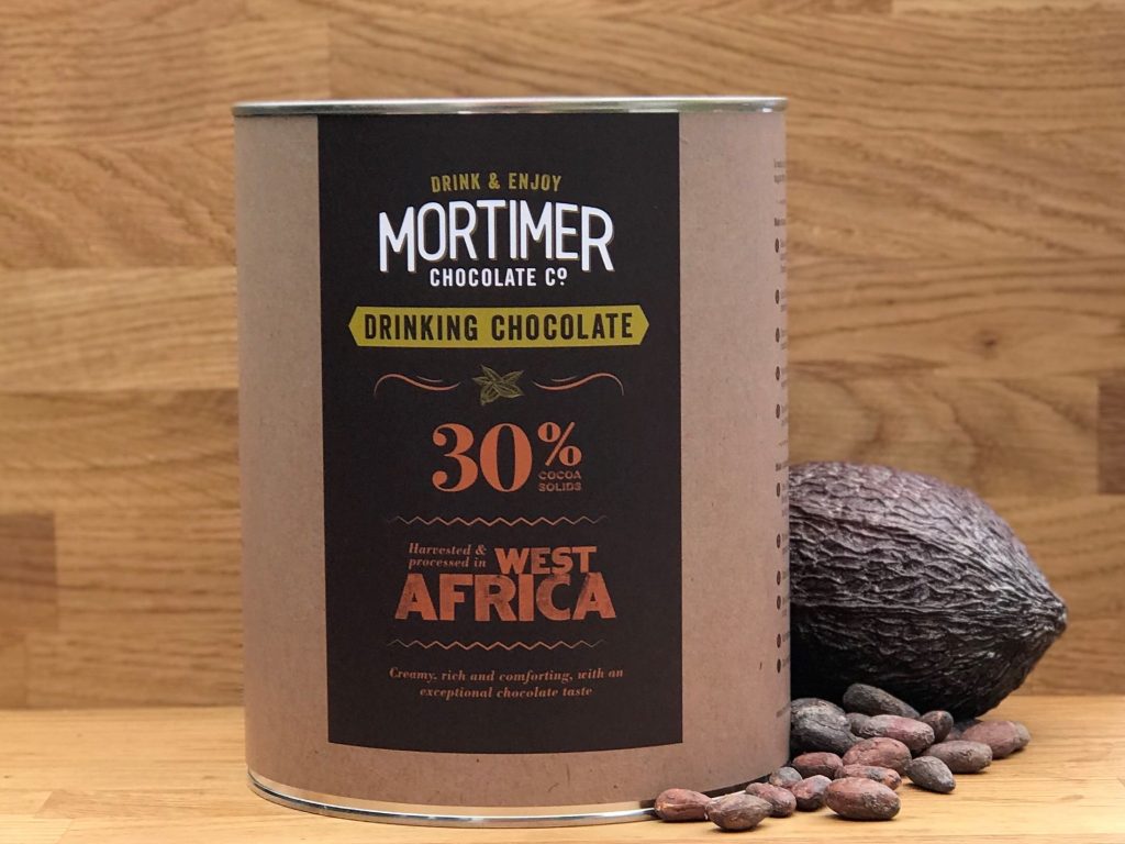 2 kg tin of 30% Drinking Chocolate sitting next to a cocoa pod and a sprinkling of cocoa beans