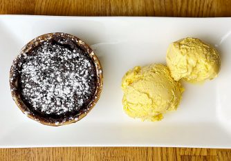 A vegan chocolate cake made in the microwave in under 2 minutes on a plate with vanilla ice cream and icing sugar