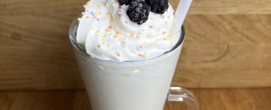 A white chocolate milkshake with squirty cream, sprinkles and frozen blackberries on it