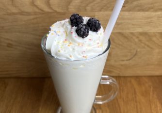 A white chocolate milkshake with squirty cream, sprinkles and frozen blackberries on it